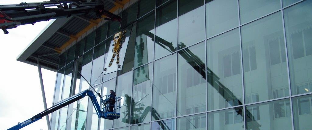 Glaszetter van Multiglas in cherrypicker brengt met hijskraan zonnewerend glas aan in grote glazen gevel. 